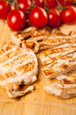 Domates yanındaki ahşap tahta üzerinde taze ızgara tavuk göğsü