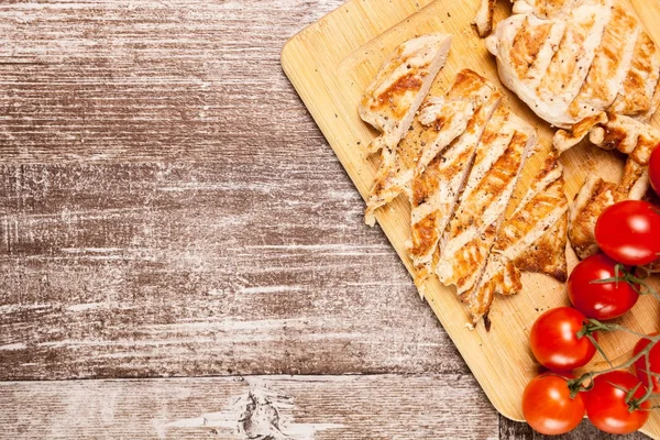 Φρέσκο ψητό στήθος κοτόπουλου στο ξύλινο πίνακα δίπλα τις ντομάτες — Φωτογραφία Αρχείου