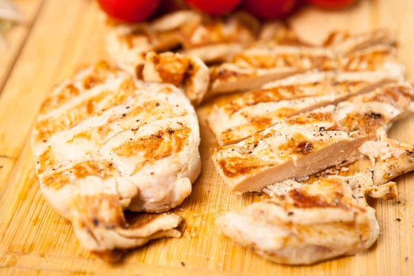 Fresh grilled chicken breast on wooden board next to tomatoes