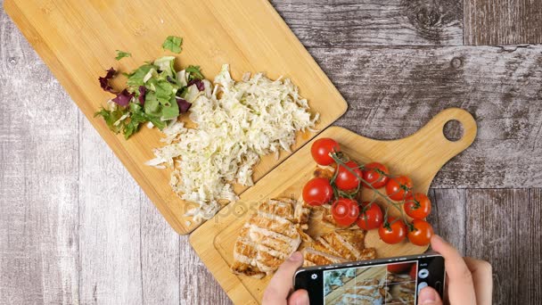 Un bloguero de comida en tomar fotos de filete de pollo con tomates y ensalada de col en el teléfono inteligente — Vídeos de Stock