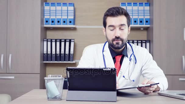 Врач использует планшетный компьютер, чтобы поговорить через видео-конференцию со своим пациентом — стоковое видео