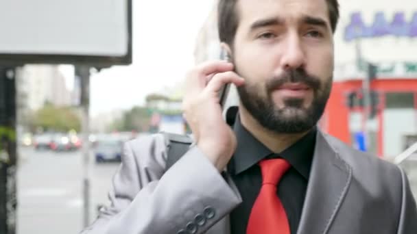 Zakenman in formele pak op straat lopen en praten over de telefoon — Stockvideo