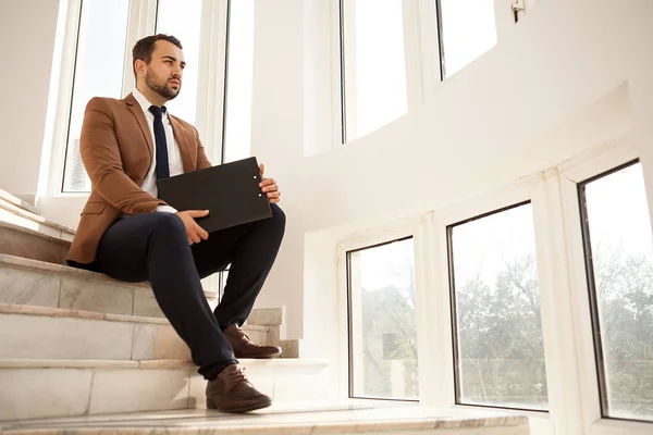 Erfolgreicher Geschäftsmann sitzt mit einem Ordner in der Hand auf der Treppe — Stockfoto