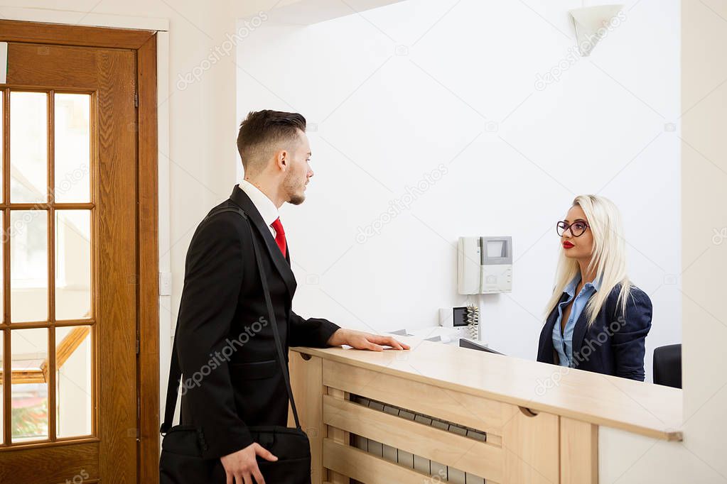 Businessman in office reception area talking with secretary