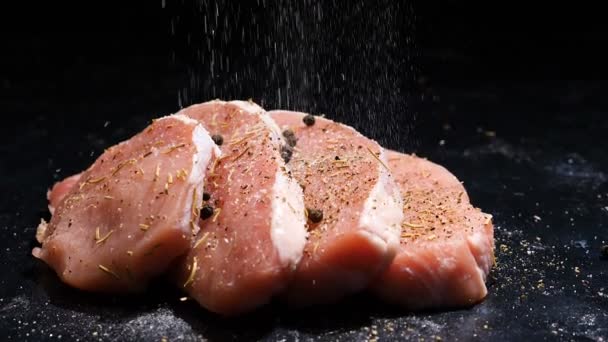 Slow motion zooming in shot on four juicy raw pices of pork steaks beeing salted — Stock Video