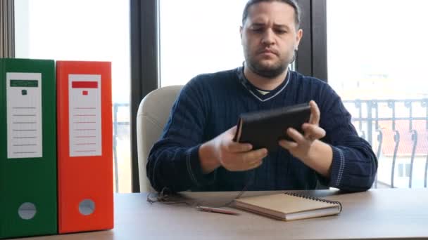 Zakenman in informele slijtage plaatsvindt achter zijn bureau en beginnen te lezen uit een oude lederen laptop — Stockvideo