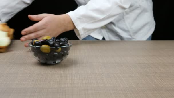 O chef organiza uma mesa composta por pedaços de queijo cortados, duas cebolas das quais uma é cortada, uma tigela de azeitona e uma salada de tomate. — Vídeo de Stock