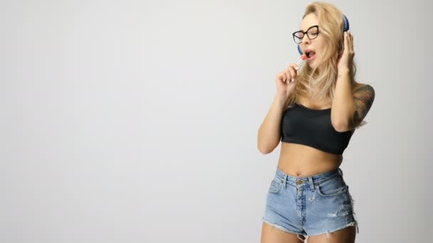 Sexy vrouw met een lolly in handen, luisteren naar muziek — Stockvideo