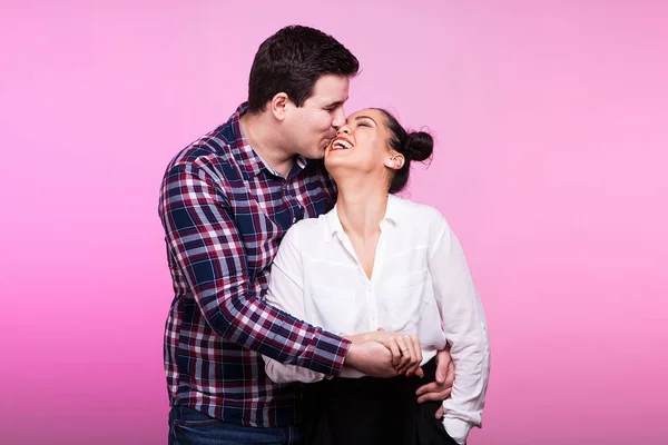 Homem abraçando e beijando uma mulher no fundo rosa — Fotografia de Stock