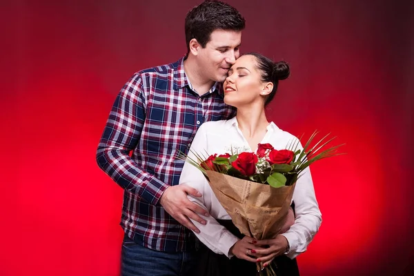 Мужчина обнимает ее жену, пока она держит букет роз в руках — стоковое фото