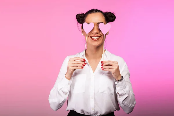 Schöne Frau, die ihre Augen mit zwei rosa Herzen auf rosa B bedeckt — Stockfoto