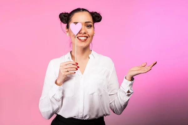Frau bedeckt ein Auge mit einem rosa Herz und zeigt mit ihrem h — Stockfoto