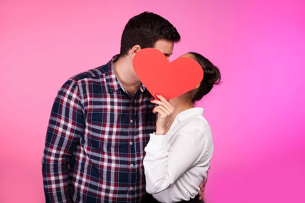 Casal beijando atrás de um coração feito de papelão — Fotografia de Stock