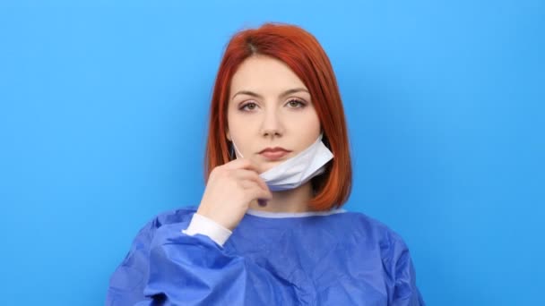 Redhead woman wearing a surgeon robe puts her mask on — Stock Video