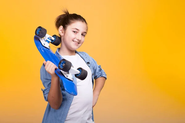 Menina adolescente legal feliz com um skate azul nas mãos — Fotografia de Stock