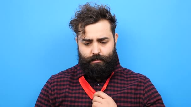 Бородатый человек пытается завязать галстук и не может этого сделать — стоковое видео