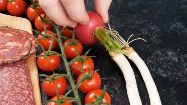 Рука кладет помидоры черри и редис рядом с тарелкой с нарезанной ветчиной и беконом — стоковое видео