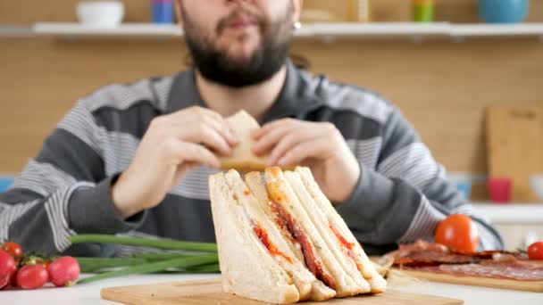 Чоловік входить на кухню, сідає і починає їсти бутерброд — стокове відео