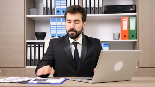 Zakenman achter zijn bureau werkt op de computer en sommige papieren — Stockvideo