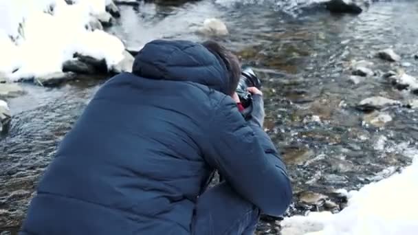 Fotograf som tar bilder av vintern river i berg — Stockvideo