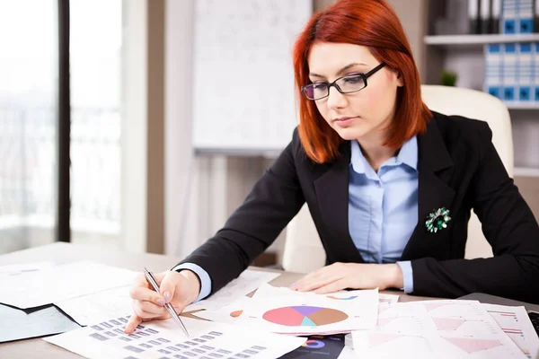 Businesswoman al suo tavolo guardando i diagrammi — Foto Stock