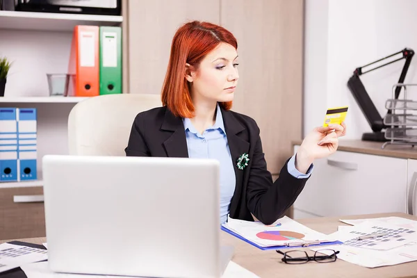 Businesswoman in her office looking at a credit card — Stock Photo, Image