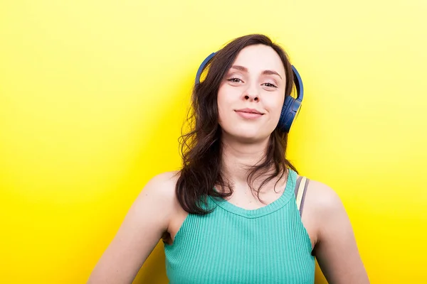 Jovem mulher olhando para a câmera enquanto ouve música em azul — Fotografia de Stock