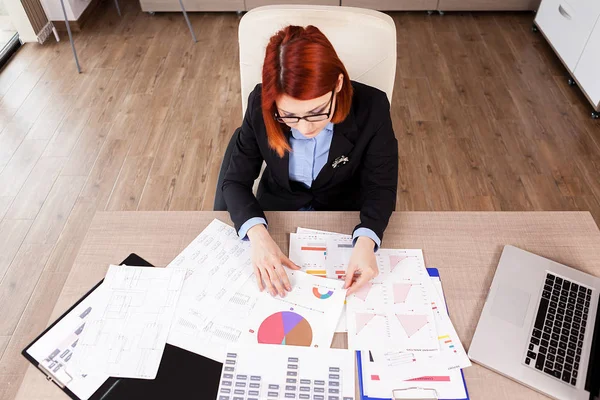Mujer en su escritorio mirando diagramas —  Fotos de Stock