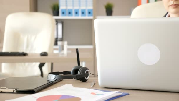 Mujer de negocios en su escritorio escribiendo y luego conectando los cables de audio y micrófono en el portátil — Vídeos de Stock