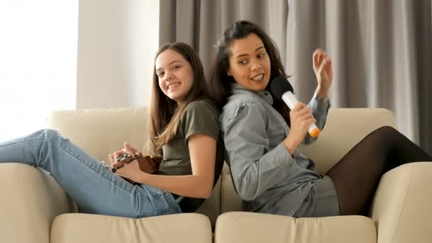 Hermanas felices y positivas tocando y cantando en el sofá — Vídeos de Stock