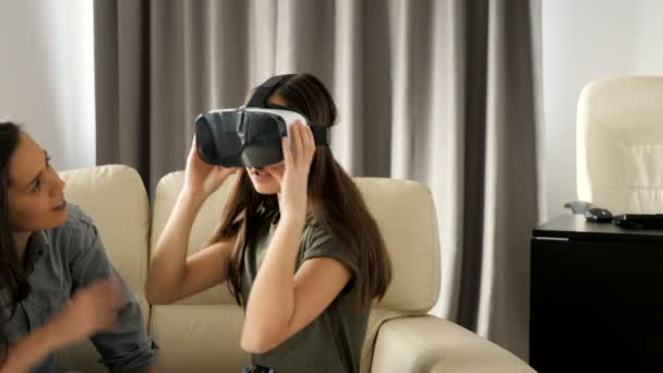 Søstre morer seg i stua på sofaen. Man opplever virtuell virkelighet for første gang – stockvideo