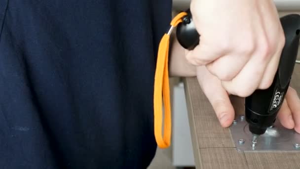 Az ember vesz egy elektromos csavarhúzót, és unscrews a csavart egy fémlemez — Stock videók