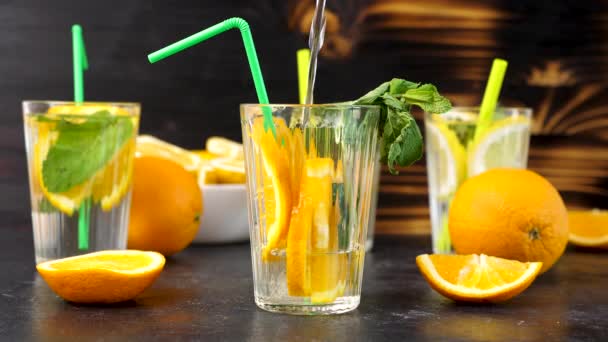 Наливание воды в стакан со свежими срезанными ломтиками апельсинов — стоковое видео