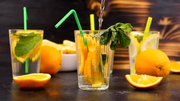 Наливание воды в стакан с ломтиками апельсинов — стоковое видео