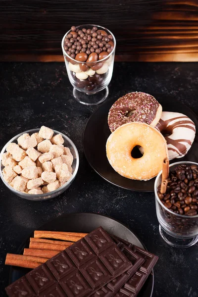 Glas met koffiebonen naast Chocoladetabletten, donuts, bruine suiker en andere glas met pinda's in chocolade — Stockfoto