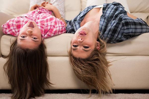 Beautiful mother with her cute daughter lying on the couch with their head upside down
