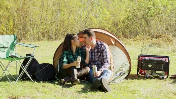 Namorado beijando sua bochecha namorada sentado na frente de sua barraca de acampamento — Vídeo de Stock
