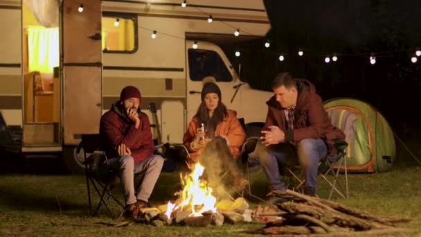 Group of friends gathered around camp fire in a cold night of autumn — Stock Video