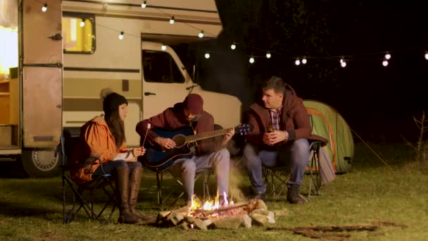 Egy férfi énekel egy dalt gitáron a barátainak a tábortűz körül. — Stock videók