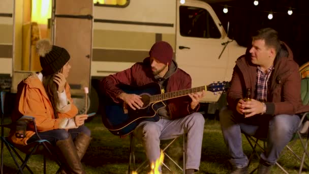 Marşmelov tutan bir kız ve arkadaşlarından biri gitarda şarkı söylüyor. — Stok video