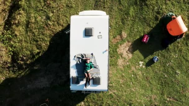 Top uitzicht van drone van mooie jonge vrouw ontspannen op de top van camper — Stockvideo