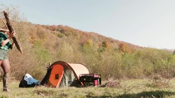 Vrienden met brandhout voor kampvuur bij de tent — Stockvideo