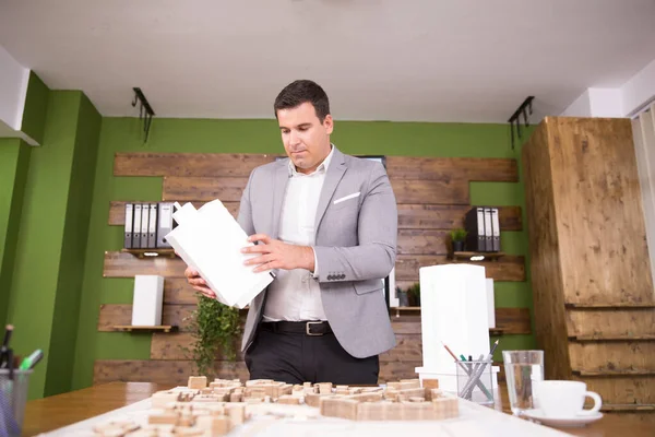 Young architect looking and holding building model in conferene room