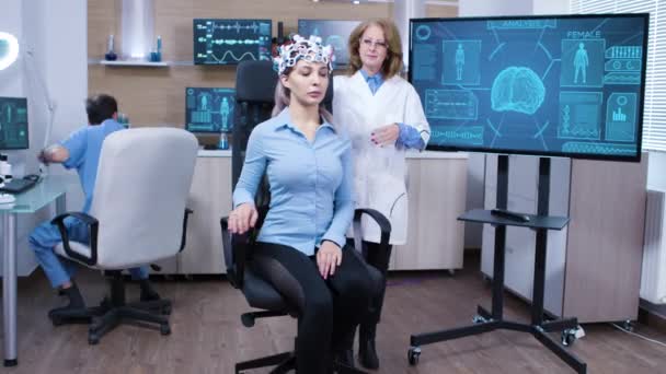 Mujer con auriculares de escaneo de ondas cerebrales sentada en una silla — Vídeo de stock