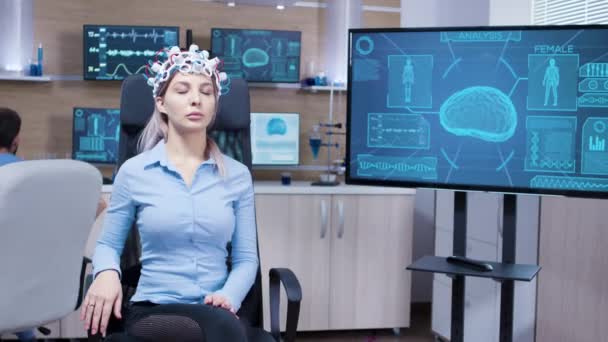 Jonge vrouwelijke patines zittend op een chiar en het dragen van hersengolven scannen headset — Stockvideo