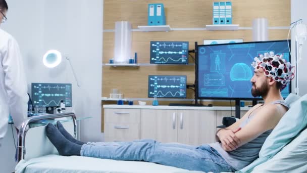 Врач в лаборатории по исследованию мозга проверяет пациента, сидящего на кровати — стоковое видео