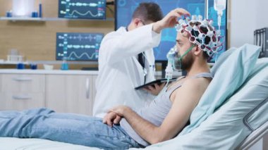 Doktor elinde tablet tutarken ve beyin sensörlerinde ayarlamalar yaparken hastaya takıldı.