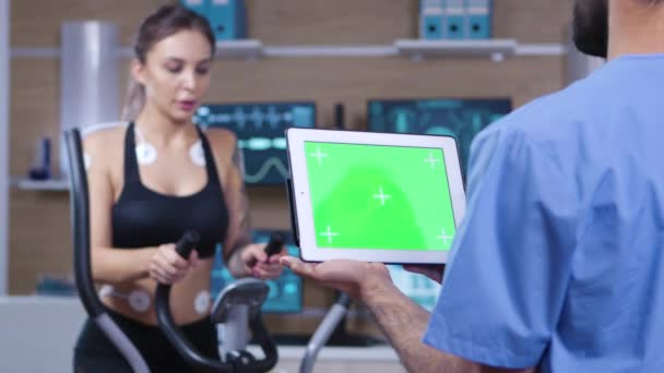 Läkare som håller tabletten med grön skärm framför idrottaren — Stockvideo