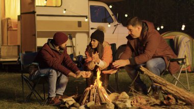 Kamp ateşi etrafında kamp sandalyelerinde oturan yakın bir arkadaş.
