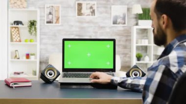 Adam yeşil ekranlı modern laptopa bakıyor.